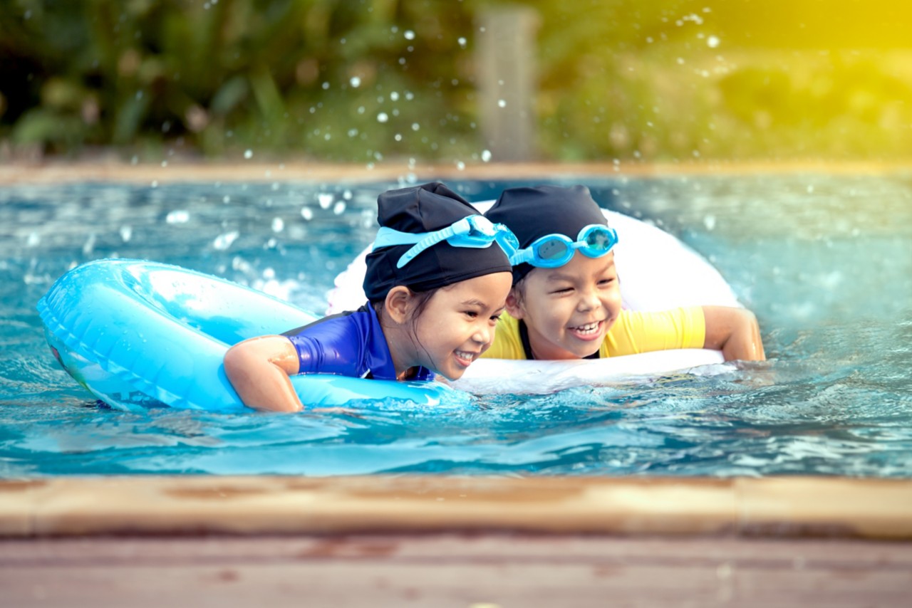 two asian little girls having fun to swim in swimming pool together