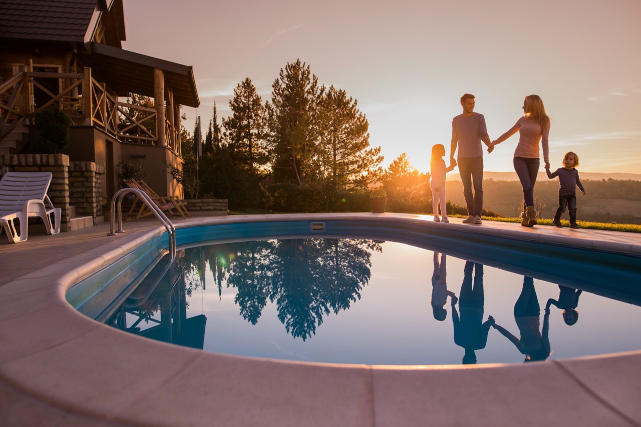 Young happy family talking while walking by outdoor pool and holding hands at sunset. 