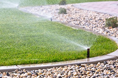 A sprinkler system watering a well-maintained lawn bordered by a stone path, showcasing efficient irrigation.