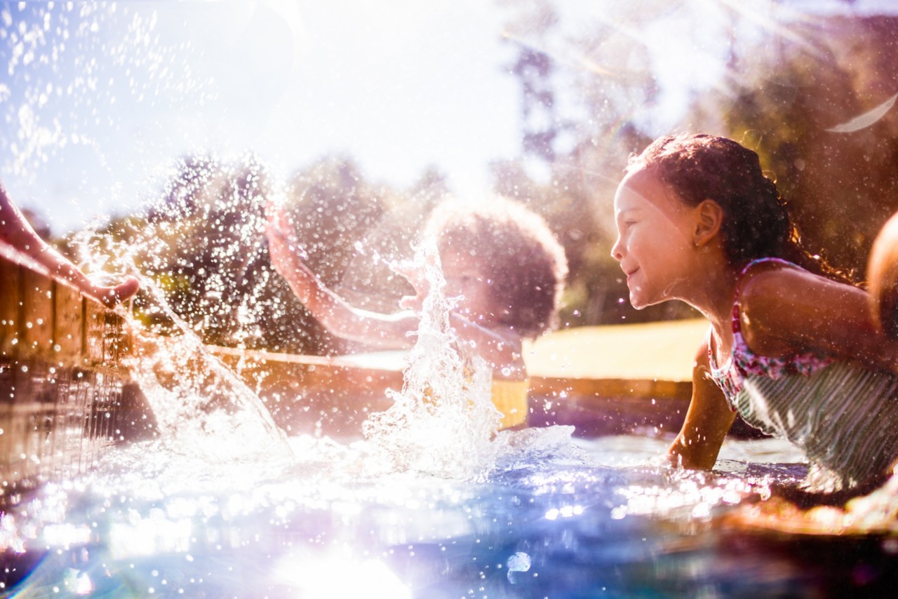 Little Afro girl with her friends splashing happily together in a pool in summer