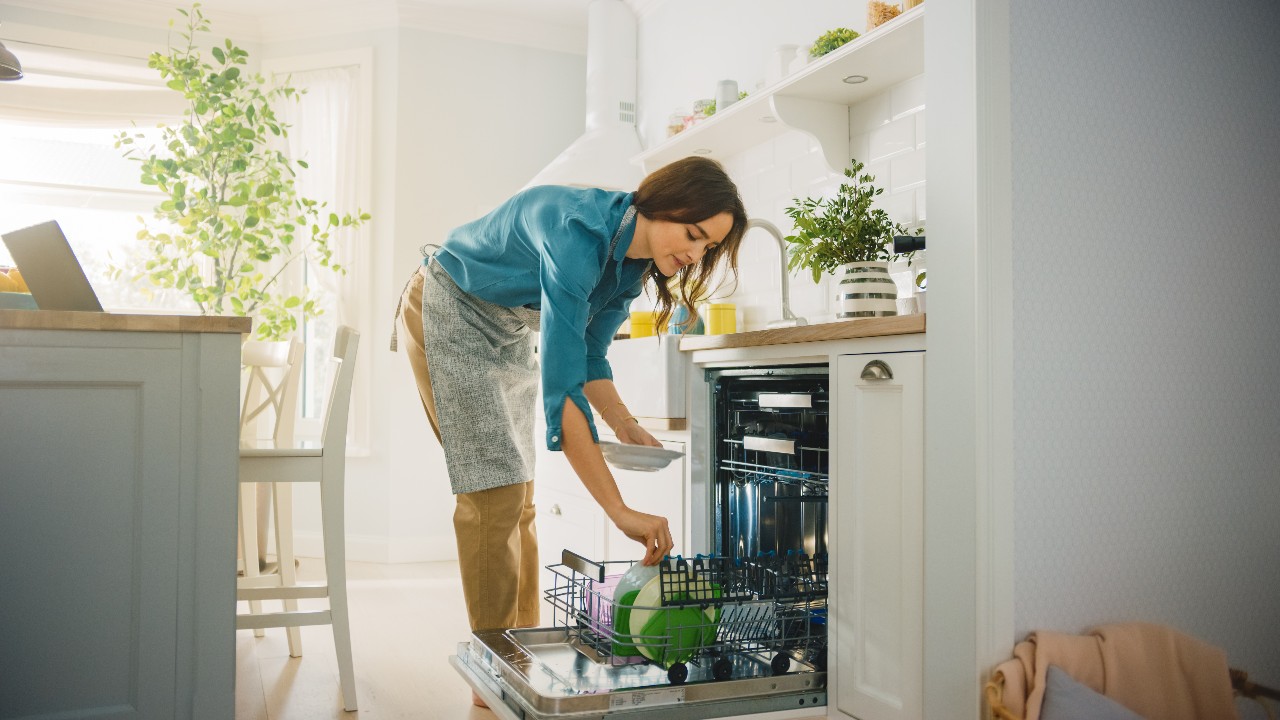 Woman loading dishes in the dishwasher in kitchen on sunny day